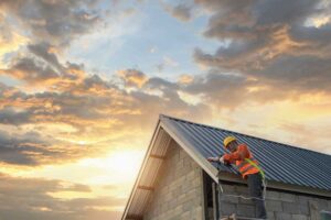 Curled and cracked asphalt shingles on a sloped roof beside a gutter and attic inspection ladder