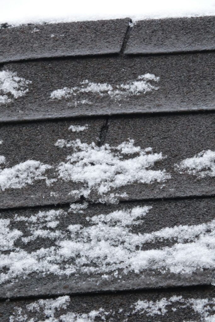 Homeowner examines scattered hail impact marks on asphalt shingles from the ground after a storm.